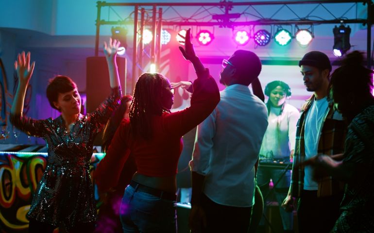Diverse persons jumping on dance floor, having fun with funky breakdance battle at nightclub. Cheerful men and women enjoying dancing party with electronic DJ music. Handheld shot.