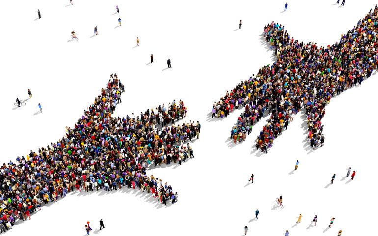 Large group of people seen from above gathered together in the shape of two hands reaching out each other