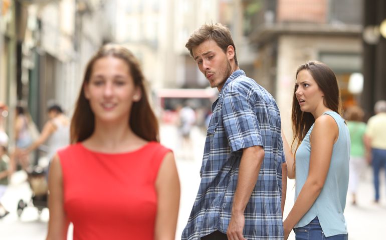 Disloyal man walking with his girlfriend and looking amazed at another seductive girl