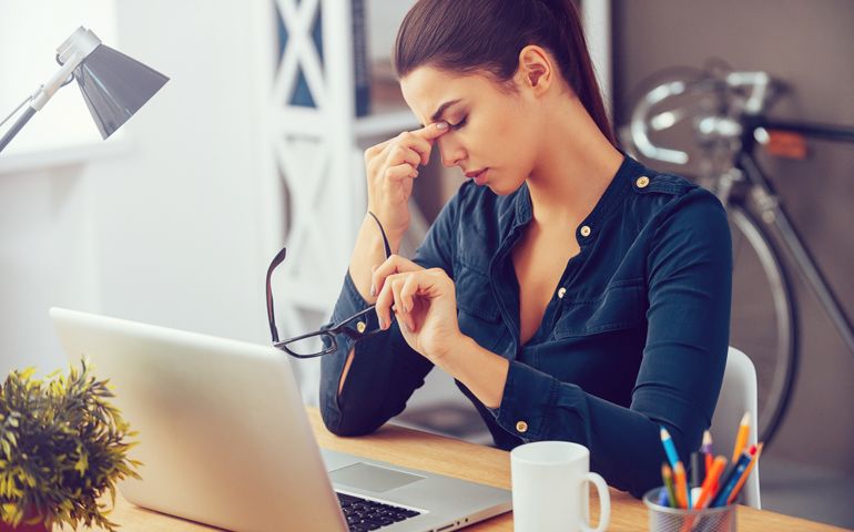 Feeling tired and stressed. Frustrated young woman keeping eyes closed and massaging nose while sitting at her working place in office