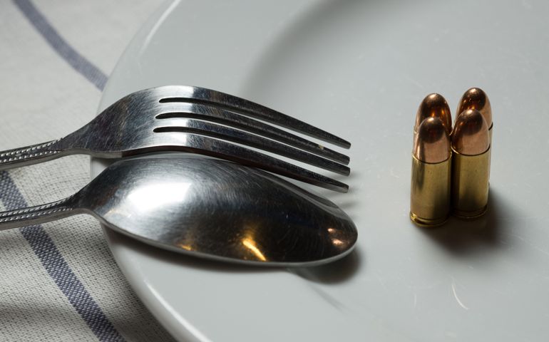 Golden bullets on a white steak dinner plate with a spoon and fork representing revenge is the dish best served cold