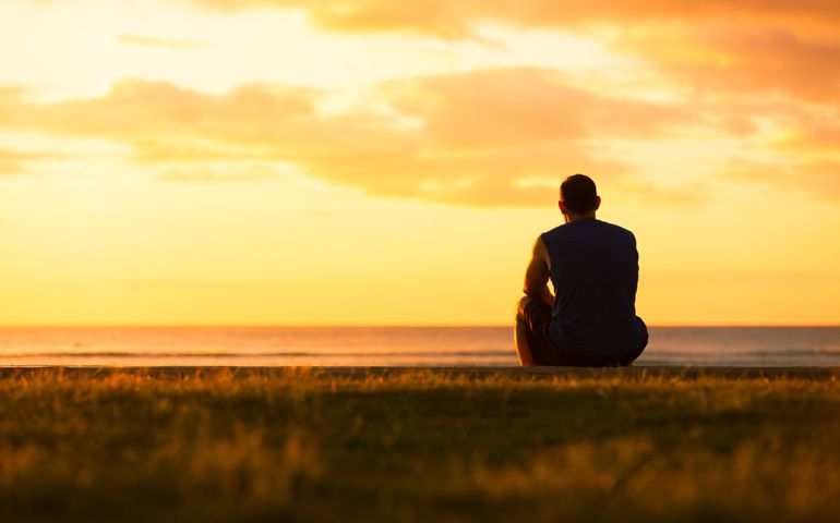 Young man sitting outdoors watching the sunset. Thinking and relaxing concept.