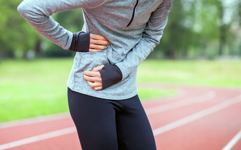 Athletic woman on running track has side cramps during workout