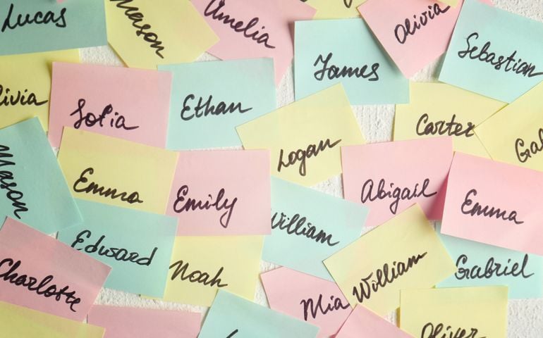 Closeup of paper stickers with different names on white wall. Concept of choosing baby name