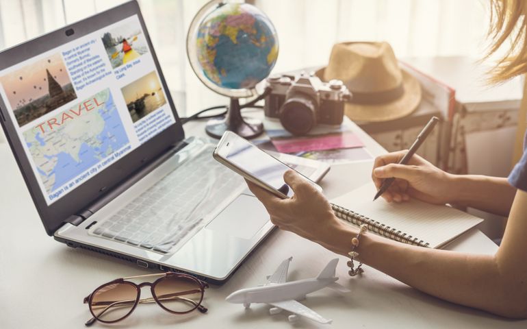 Young woman planning vacation trip and searching information or booking an hotel on a smart phone and laptop, Travel plan concept