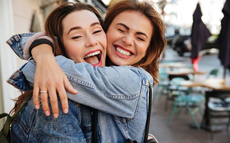 Close-up photo of laughing woman friends hugging each other on city street