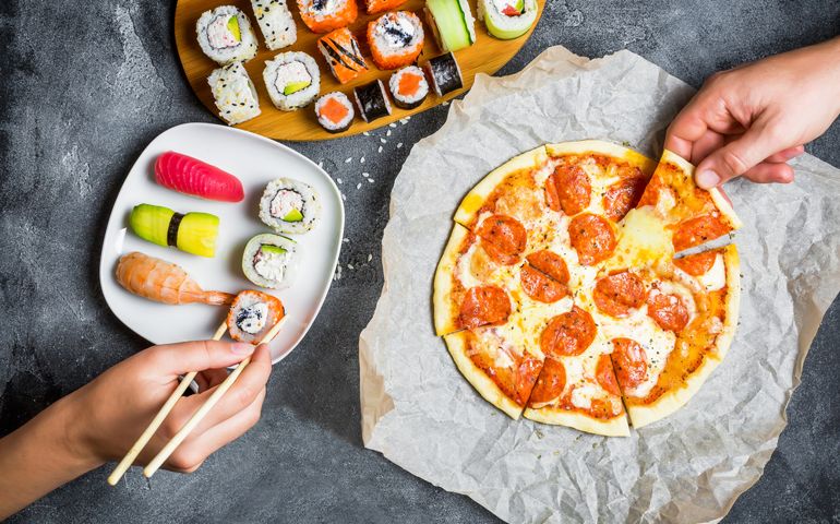 Pizza with salami, set of sushi rolls and hands take food. Food background. Flat lay, top view.