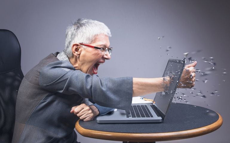 Crazy enraged senior business woman punching through her laptop, frustrated because it doesn't work properly