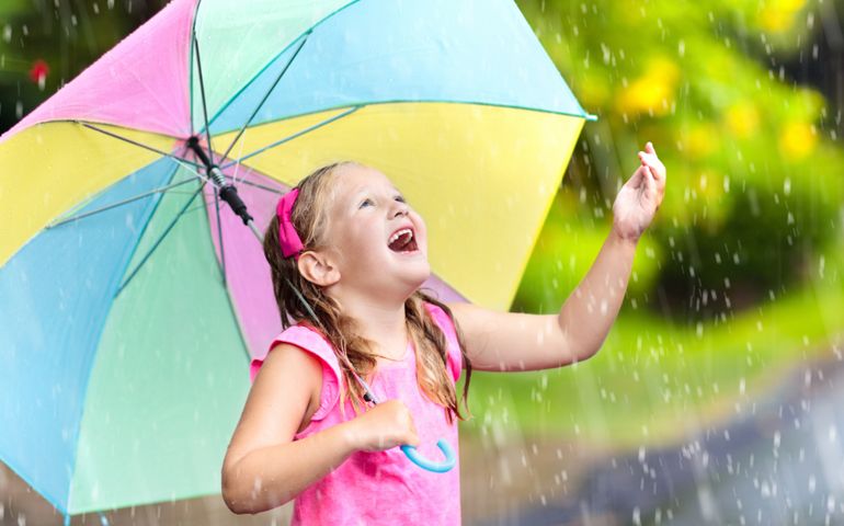 Kid playing out in the rain. Child with umbrella play outdoors in heavy rain. Little girl caught in spring shower.