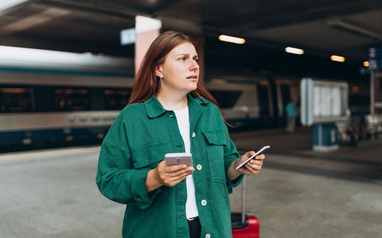 Young refugee redhhead woman crying and waiting train on station platform, she lost and using smart phone. Railroad transport concept, Traveler.