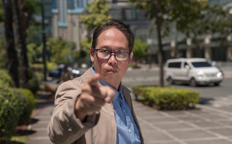 A self righteous and nosy asian man warns someone to back off. Pointing with his finger, looking furious. Outdoor city scene.