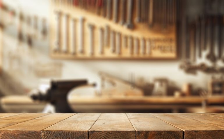Worn old wooden table and workshop interior. Retro vintage photo of background and mockup. Sun light and dark shadows.