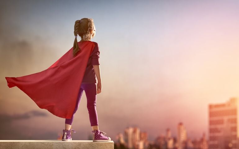 Little child girl plays superhero. Child on the background of sunset sky. Girl power concept