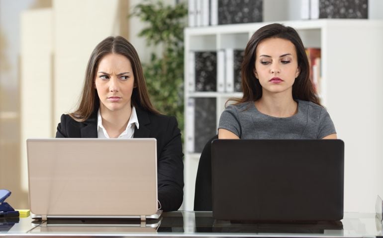 Front view of two angry businesswomen looking each other with hate working with laptops at office