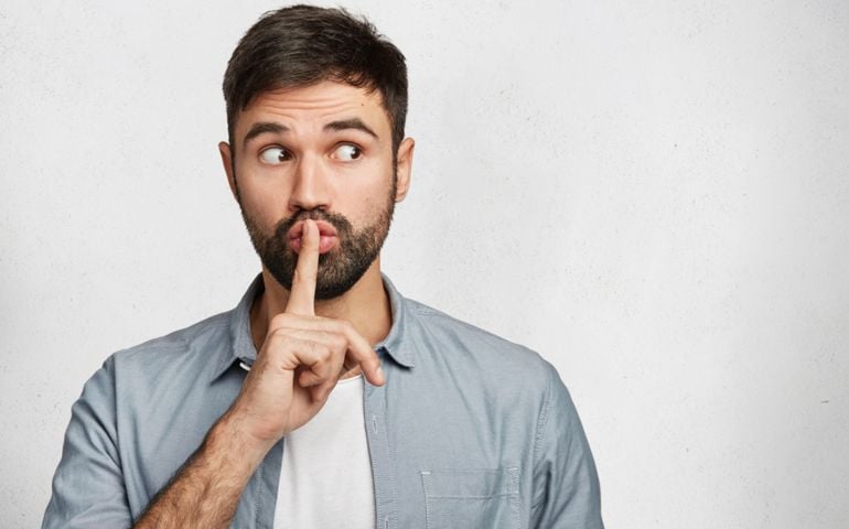 Serious good looking male with trendy hairdo, keeps fore finger on lips, tries to keep conspiracy, looks aside, says: Shh, make silence please. Isolated shot of attractive man shows silence sign