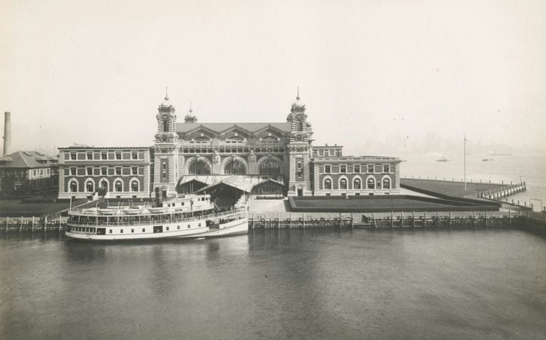 An excellent view of the front facade of the Immigration Station; a boat is docked in front. Ellis Island.