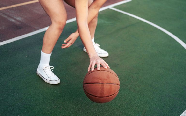 A close-up of a basketball player dribbling on an outdoor court, wearing white sneakers and socks, capturing the intensity and movement of the game.