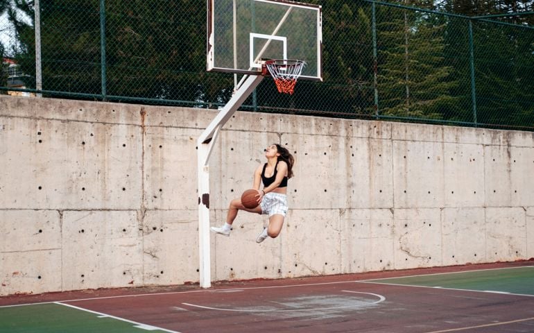 A female basketball player leaps into the air for a layup on an outdoor court, her focus locked on the hoop as she prepares to score.
