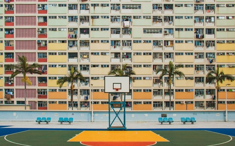 A colorful outdoor basketball court set against the backdrop of a vibrant, densely packed apartment building, creating a striking urban scene.
