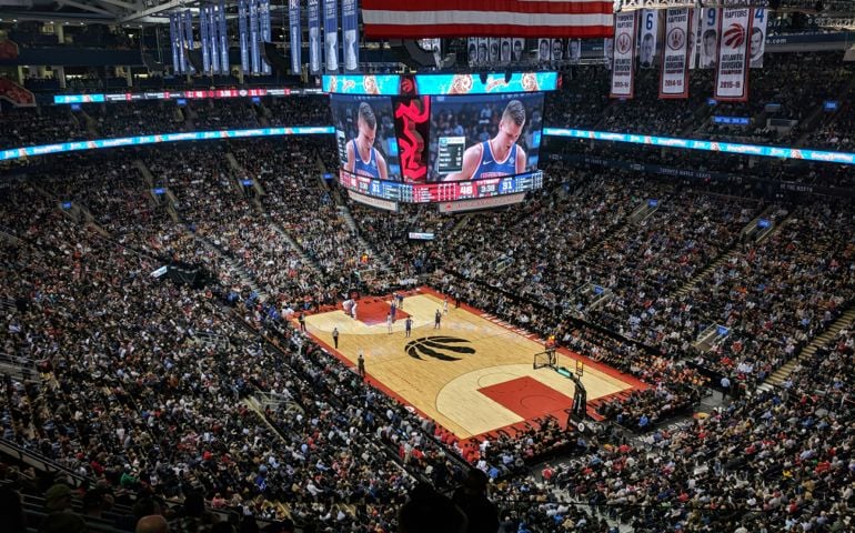 A packed basketball arena captures the excitement of a live NBA game, with thousands of fans watching as players compete on the Toronto Raptors’ home court at Scotiabank Arena.