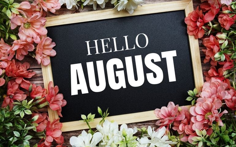 A blackboard sign framed by pink and white flowers reads “HELLO AUGUST”—a nod to August’s blend of summer warmth and quietly historic moments, from iconic festivals to meteor showers.