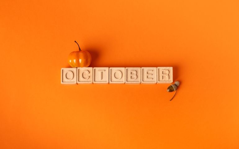 A small pumpkin and an acorn frame wooden tiles spelling “October” on a bold orange background—hinting at the month’s mix of autumn rituals, Halloween excitement, and milestone moments.